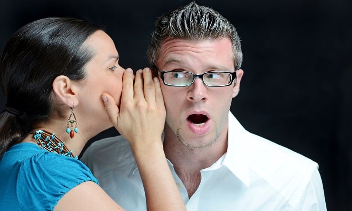 A woman whispering into a surprised man's ear.