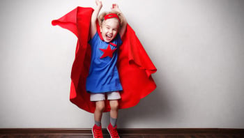 Happy child in superhero suit against gray wall.