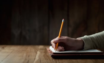 Closeup of woman’s hand writing on paper over wooden table