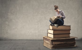 Young woman reading while sitting on a pile of books