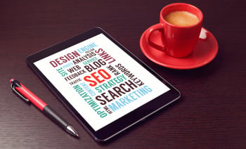 Digital tablet with SEO words and coffee cup on office desk