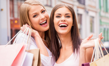We love shopping together. Two happy young women holding shopping bags and smiling while standing outdoors