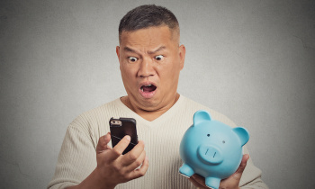 Shocked man looking at his smart phone holding piggy bank