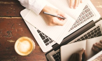 Man hands writing in the diary, coffee mug and laptop on wooden table