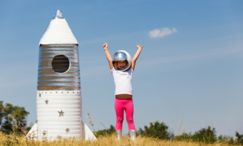 Happy child dressed in an astronaut costume playing with hand made rocket. Summer outdoor