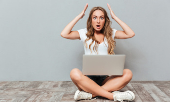 Shocked astonished woman sitting with legs crossed and holding laptop