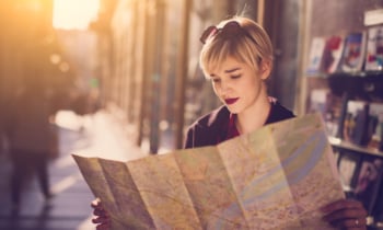 Young beautiful female traveler standing on the street and looking at the map