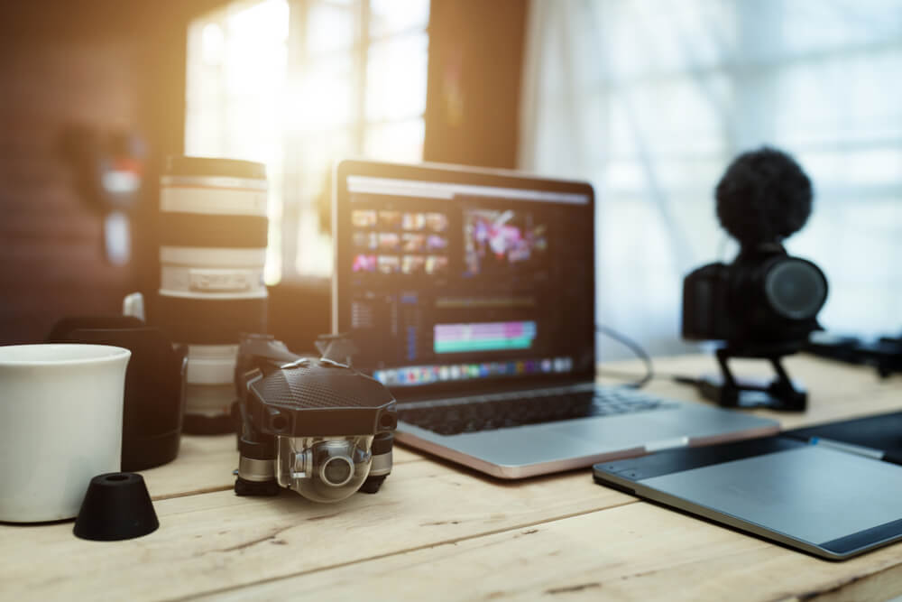 laptop com ediçao de video em tela sob mesa com materiais de video em sua volta