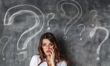 puzzled young brunette woman in glasses surrounded question marks