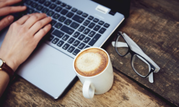 Woman hands on keypad at wooden table with fresh hot coffee. Concept of distance work and creativity.