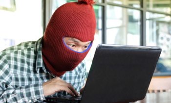 Masked hacker wearing a balaclava stealing data from laptop. Internet security concept.