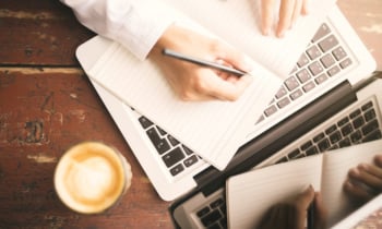 Man hands writing in the diary, coffee mug and laptop on wooden table