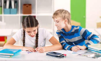 Schoolgirl writing a test and boy looking at her copybook