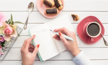 Woman hands drawing or writing with ink pen in open notebook on white wooden table. Bird eye view.