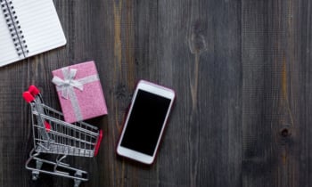 Mobile shopping. Shopping cart, phone, gift box on dark wooden background top view copyspace