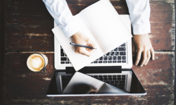 Man writing in notepad with laptop and coffee mug on wooden table
