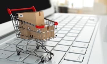 E-commerce. Shopping cart with cardboard boxes on laptop.