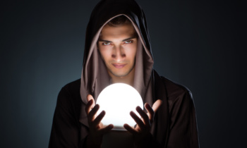 Young wizard with crystal ball in dark room