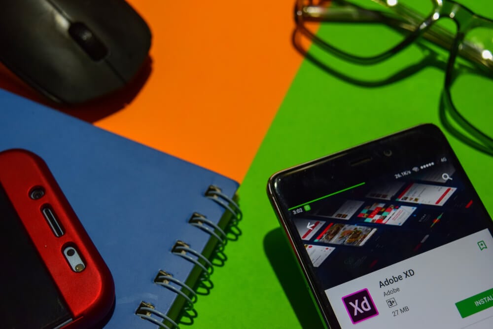 cadernos, mouse e smartphone em tela de download do app Adobe XD