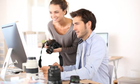 homem ao computador e mulher segurando câmera fotográfica