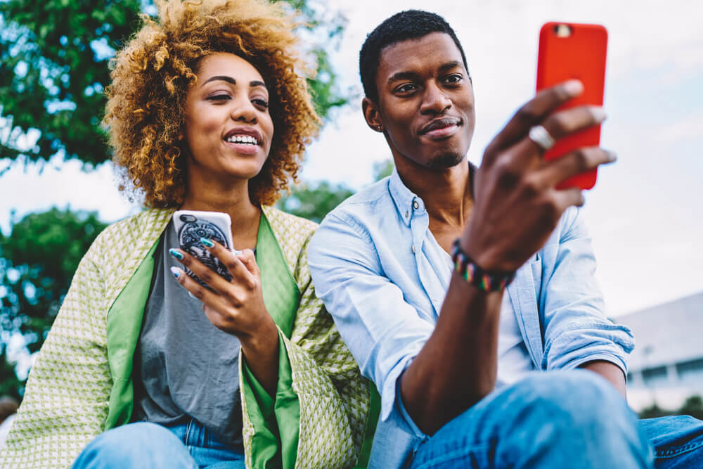 homem e mulher alegres acessando seus smartphones
