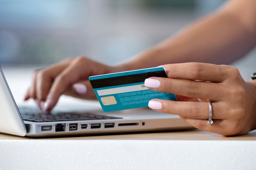 mão feminina acessando laptop com cartão de crédito em mãos