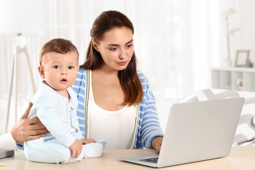 mulher acessando laptop em mesa enquanto cuida de bebê