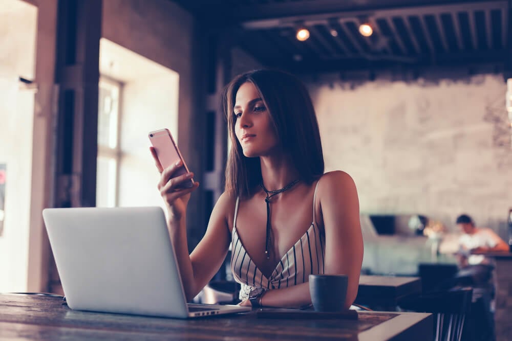 mulher ao smartphone enquanto trabalha no laptop