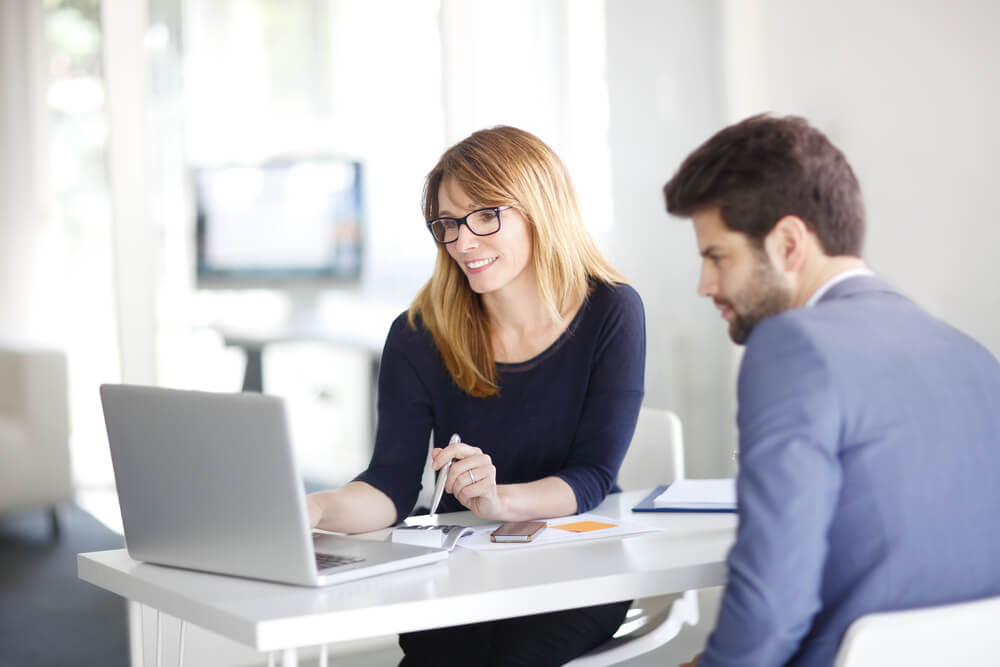 mulher mostrando algo em laptop para homem em ambiente corporativo