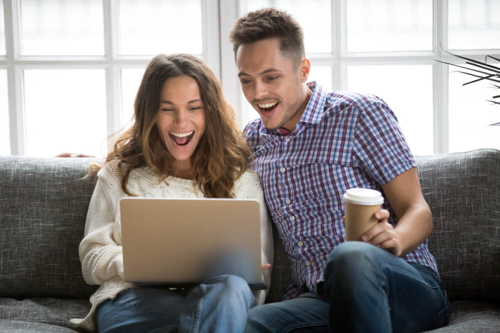casal sorridente e animado em frente a laptop
