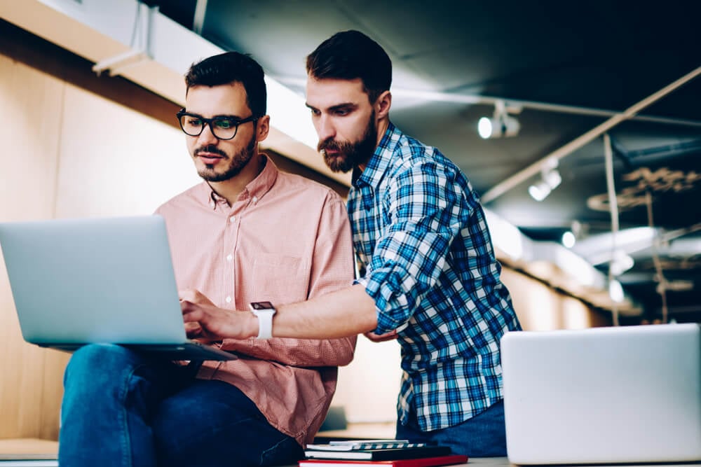 dupla de colegas de trabalho se ajudando em trabalho em laptop