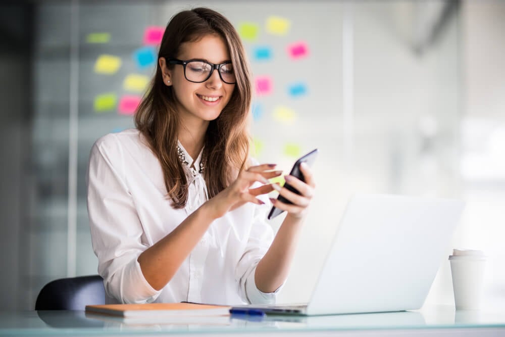 garota segurando smartphone em mesa executiva com laptop e sua frente