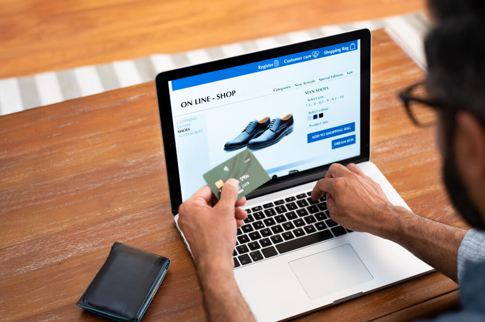 homem acessando loja omnichannel de sapatos no laptop e segurando cartão de crédito