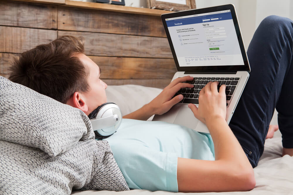 homem deitado acessando laptop na plataforma Facebook