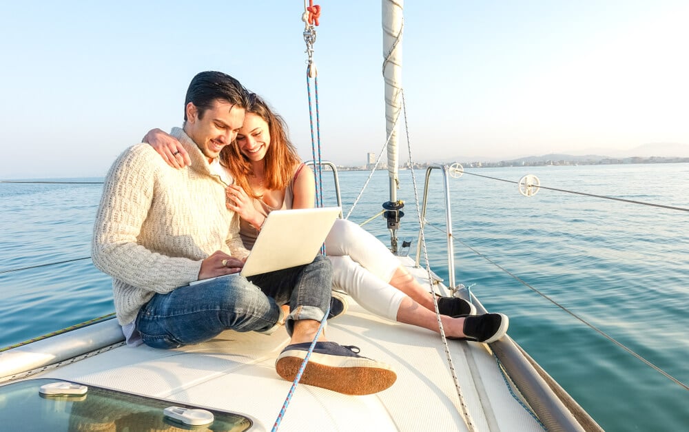 homem nomade digital e companheira em barco em meio ao oceano focados em laptop