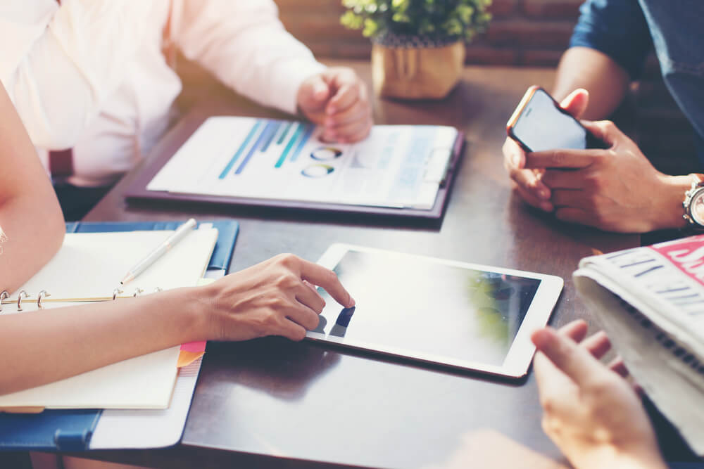 mãos de pessoas de equipe analisando e criando gráficos e cronogramas em tablet sob mesa