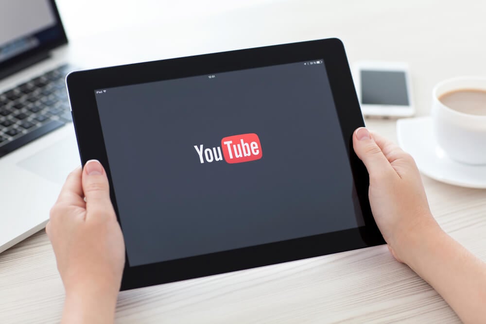 maos segurando tablet com a logo do aplicativo youtube em tela