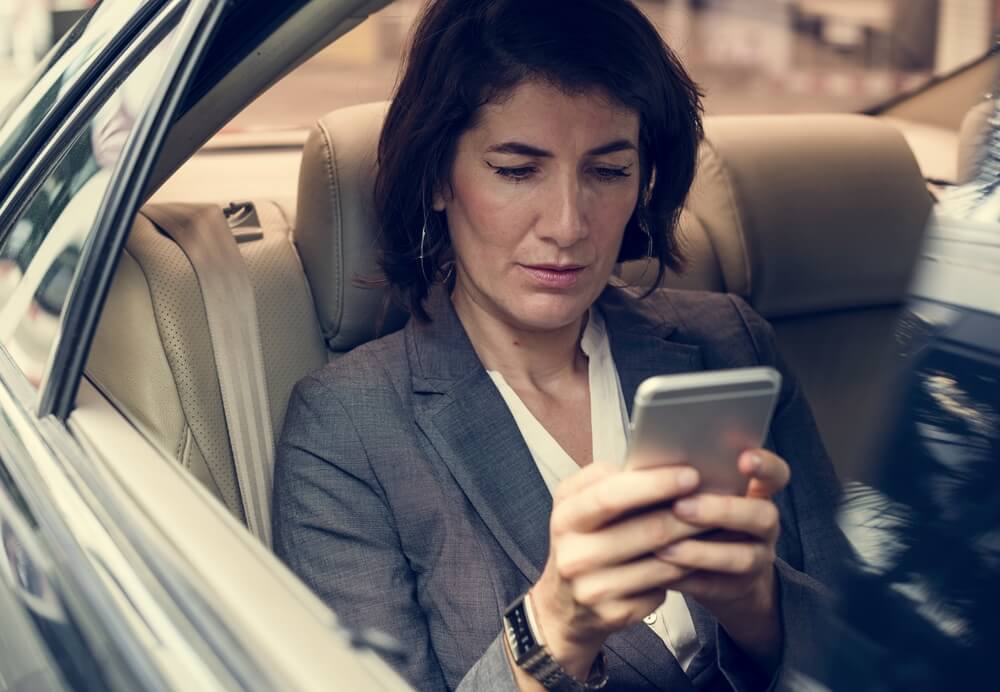 mulher execuriva segurando smartphone dentro de carro