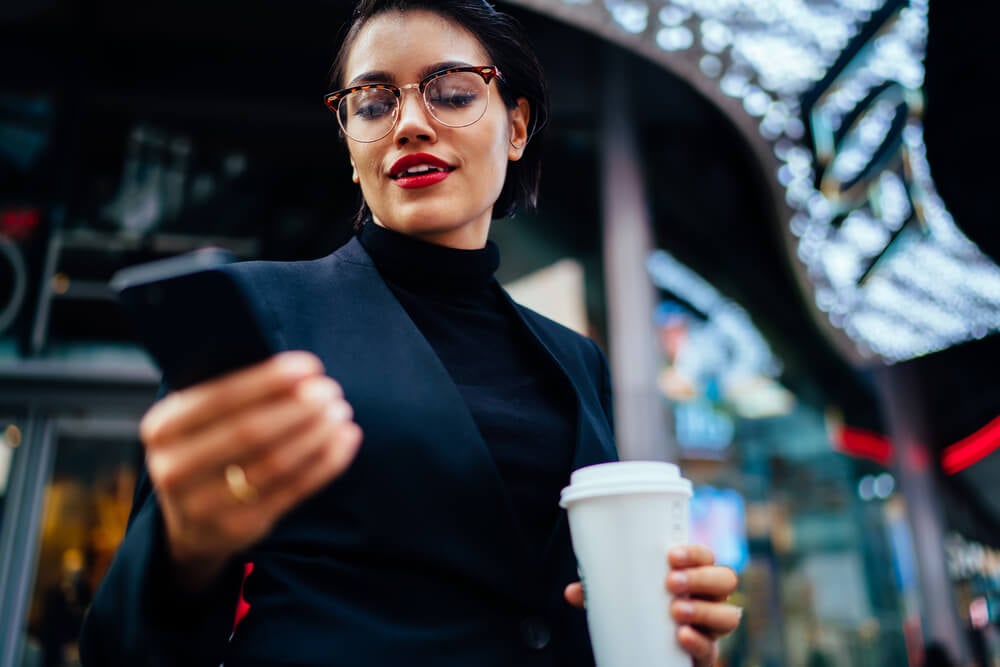 mulher executiva fazendo checkin em smartphone e segurando copo de café