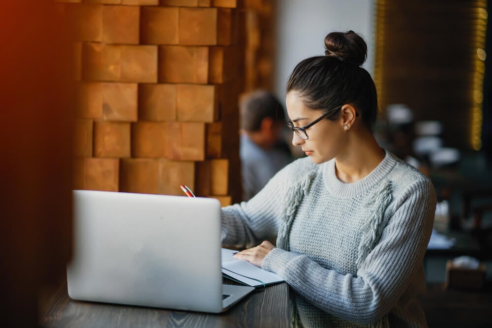 mulher profissional fazendo anotações em frente a laptop em ambiente informal