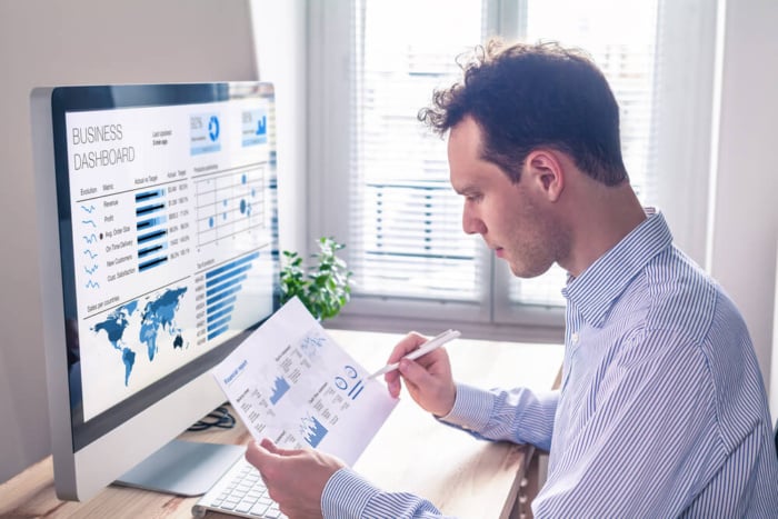 homem segurando papel em frente a computador, analisando o ticket médio
