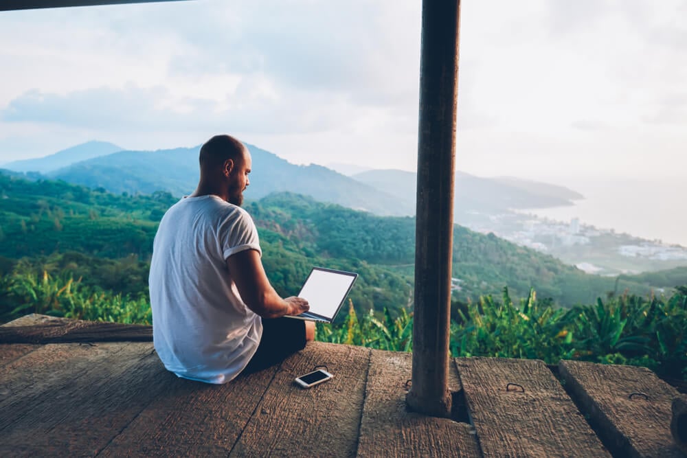 profissional de trabalho remoto sentado em sacada com paisagem de fundo