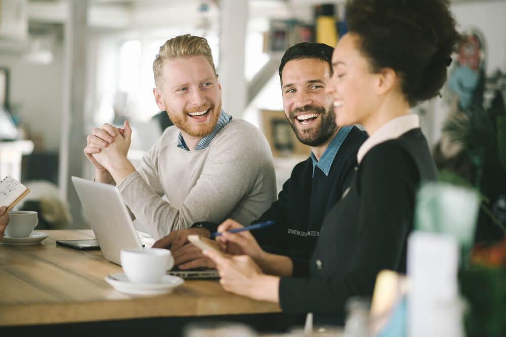 trio de colegas de trabalho sorridentes em mesa de café