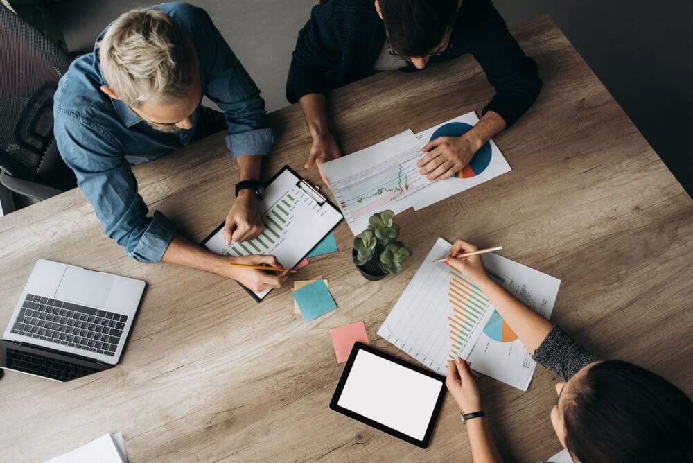 visão de cima de mesa com equipe de administração de marketing e papéis com gráficos