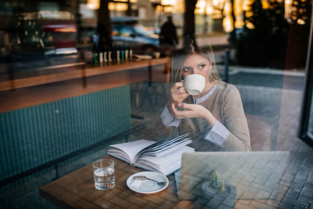 garota em café lendo livro em frente a laptop