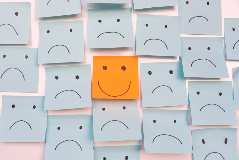 ilustraçao notas coladas em parede com rostos tristes ao redor de nota com rosto feliz