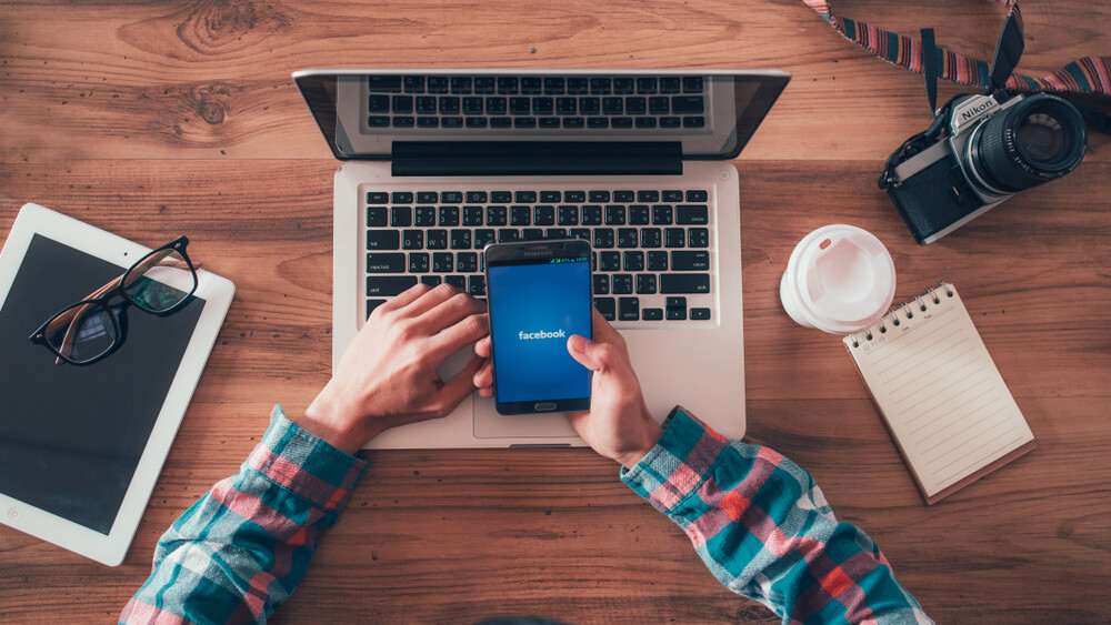 mãos masculinas segurando smartphone junto de laptop câmera e tablet