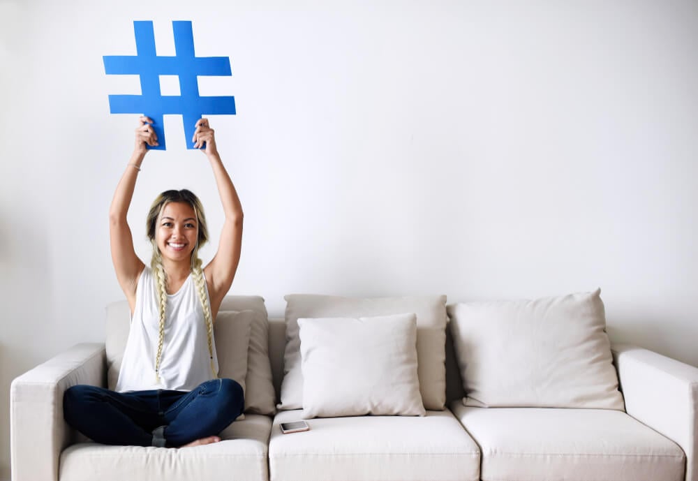 mulher sentada em sofá segurando grande símbolo de hashtag