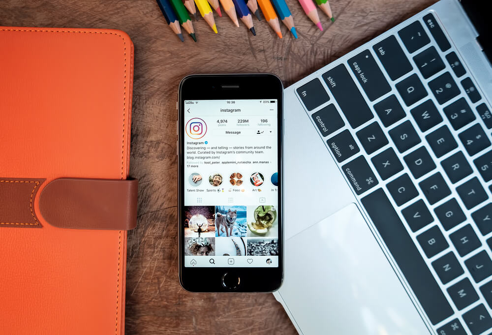página do aplicativo Instagram em smartphone sob mesa junto de laptop 