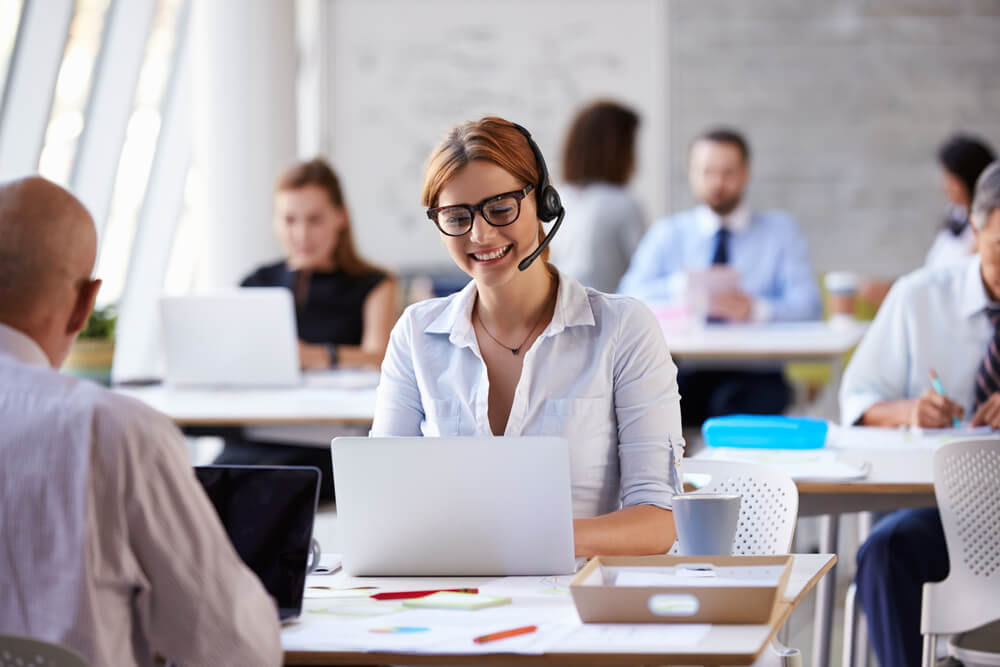 profissional em vendas por telemarketing sorrindo ao teclar em laptop em seu olocal de trabalho